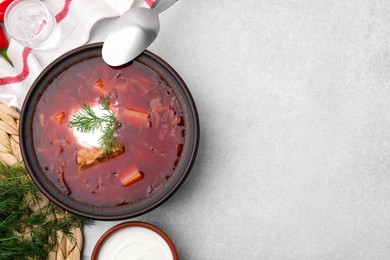 Photo of Tasty borscht with sour cream in bowl served on grey table, flat lay. Space for text