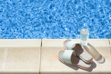 Photo of Stylish slippers and glass of water near outdoor swimming pool on sunny day, space for text