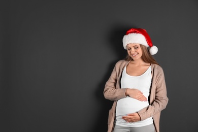 Photo of Young pregnant woman in Santa hat on grey background, space for text. Christmas celebration
