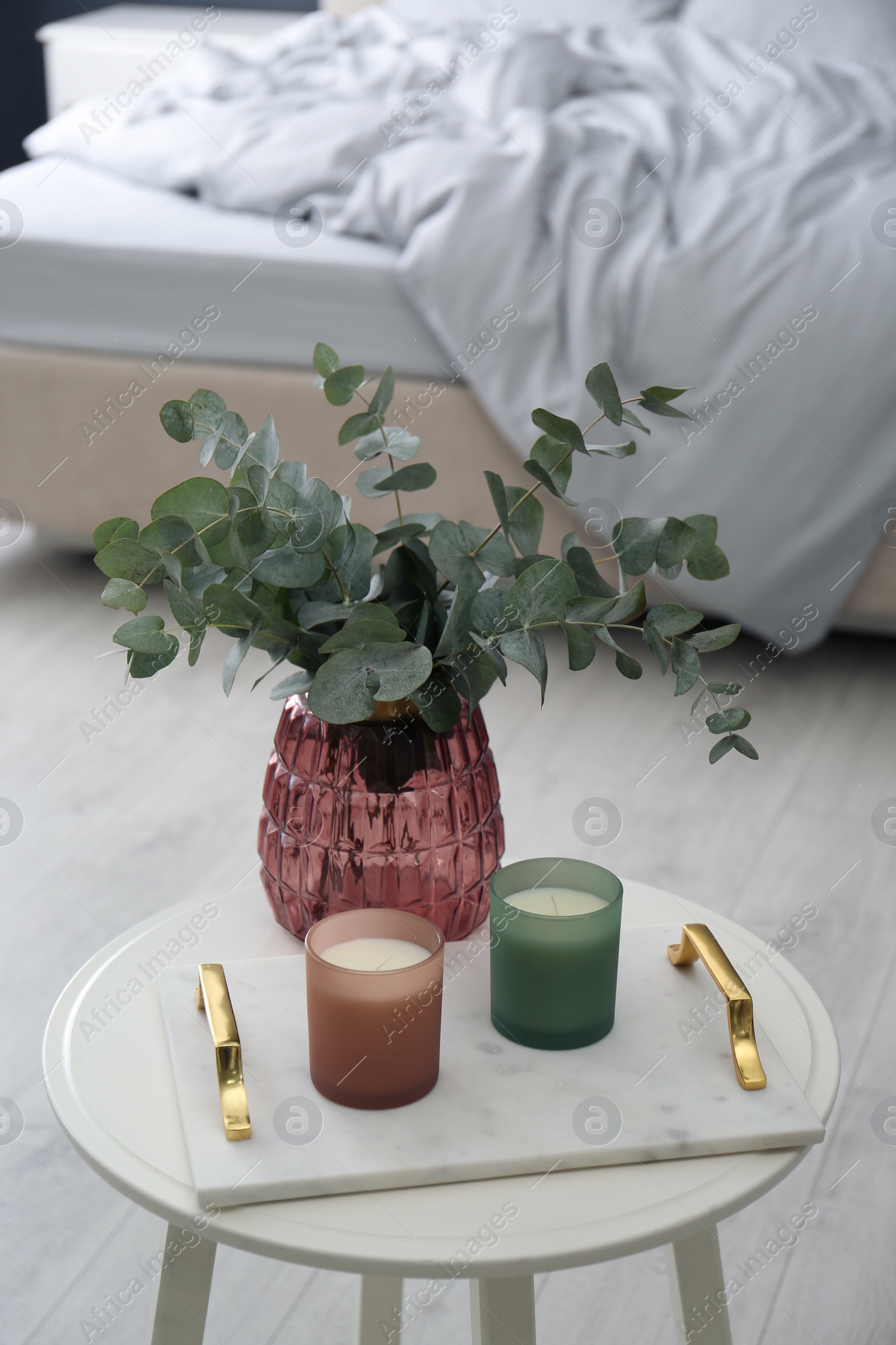 Photo of Candles and eucalyptus branches on white table in bedroom. Interior element