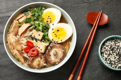 Photo of Noodle soup. Bowl of delicious ramen, ingredients and chopsticks on black table, top view