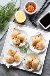 Photo of Raw scallops with spices, lemon zest, dill, shells and sauces on grey marble table, flat lay