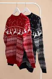 Rack with different Christmas sweaters on beige background