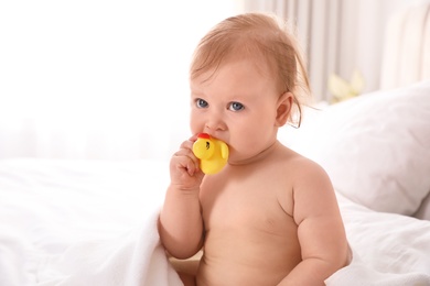 Photo of Cute little baby nibbling toy on bed after bath