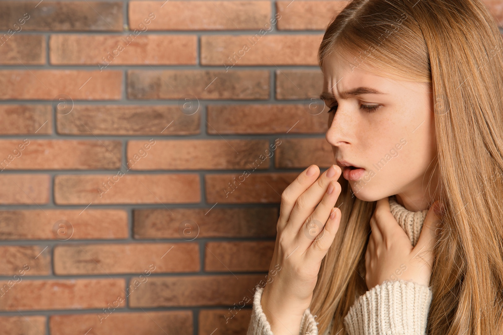 Photo of Teenage girl suffering from cough near brick wall. Space for text