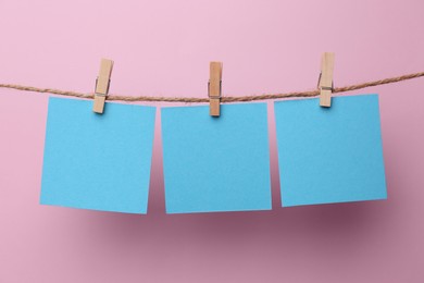 Photo of Wooden clothespins with blank notepapers on twine against pink background. Space for text