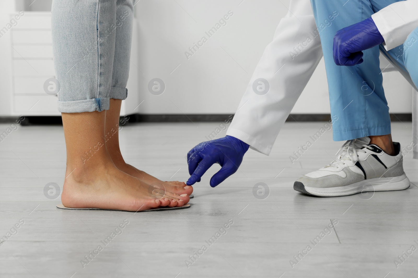 Photo of Male orthopedist fitting insoles to patient's feet in hospital, closeup