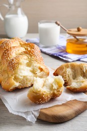 Photo of Broken homemade braided bread with sesame seeds on wooden table. Traditional Shabbat challah