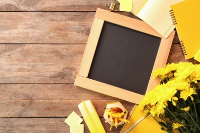 Photo of Blackboard, stationery and flowers on wooden table, flat lay with space for text. Teacher's Day