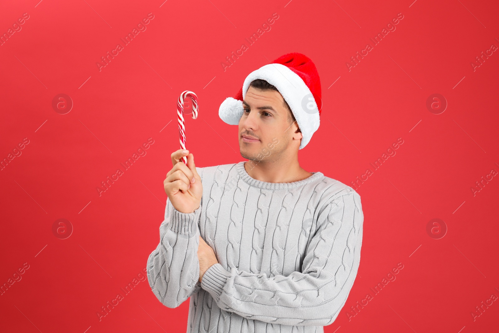 Photo of Handsome man in Santa hat holding candy cane on red background