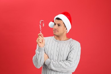 Photo of Handsome man in Santa hat holding candy cane on red background