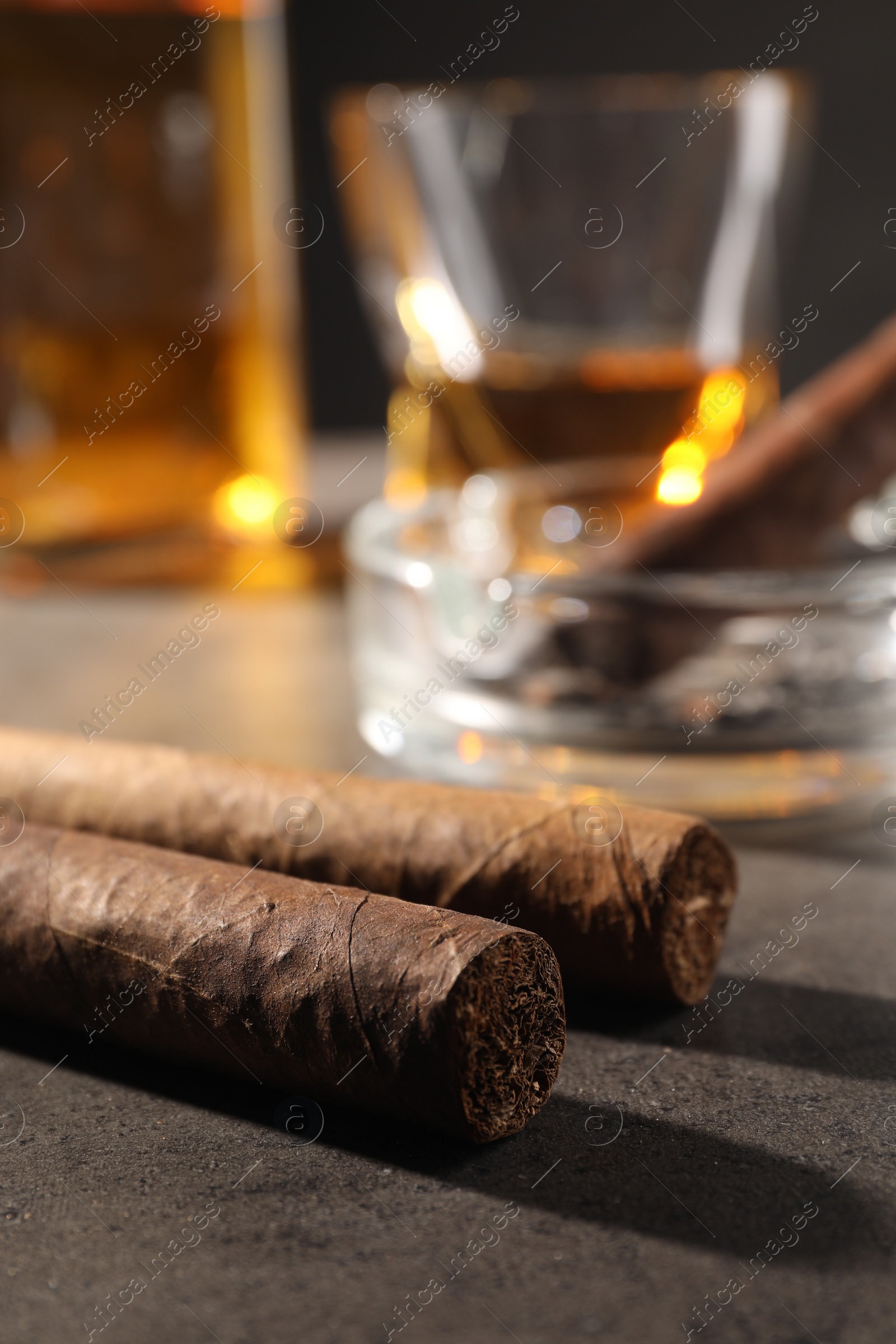 Photo of Cigars, ashtray and whiskey on grey table, closeup