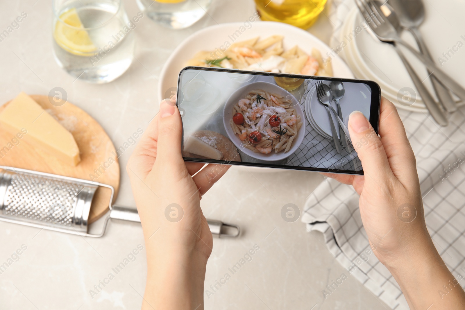 Photo of Food blogger taking picture of tasty pasta with shrimps and tomatoes at light table, closeup