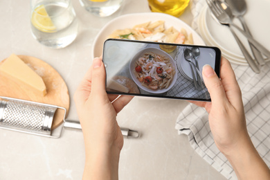 Food blogger taking picture of tasty pasta with shrimps and tomatoes at light table, closeup