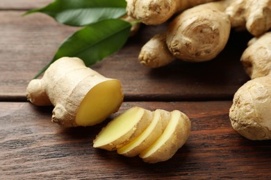 Photo of Cut and whole fresh ginger with leaves on wooden table, closeup