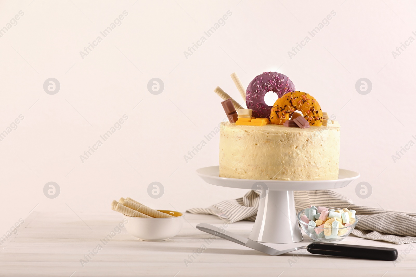 Photo of Delicious cake decorated with sweets, wafer rolls, marshmallows and pie server on white wooden table, space for text