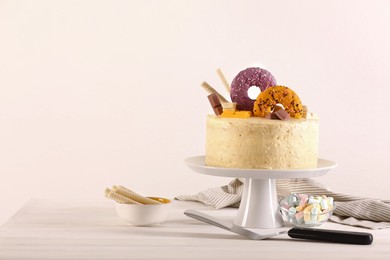 Photo of Delicious cake decorated with sweets, wafer rolls, marshmallows and pie server on white wooden table, space for text