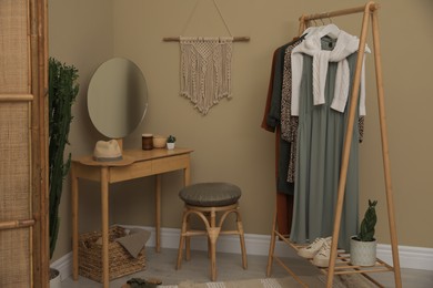 Photo of Modern dressing room interior with clothing rack, wooden table and mirror