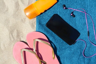 Photo of Soft blue beach towel with bottle of sunscreen, smartphone, earphones on sand, flat lay. Space for text