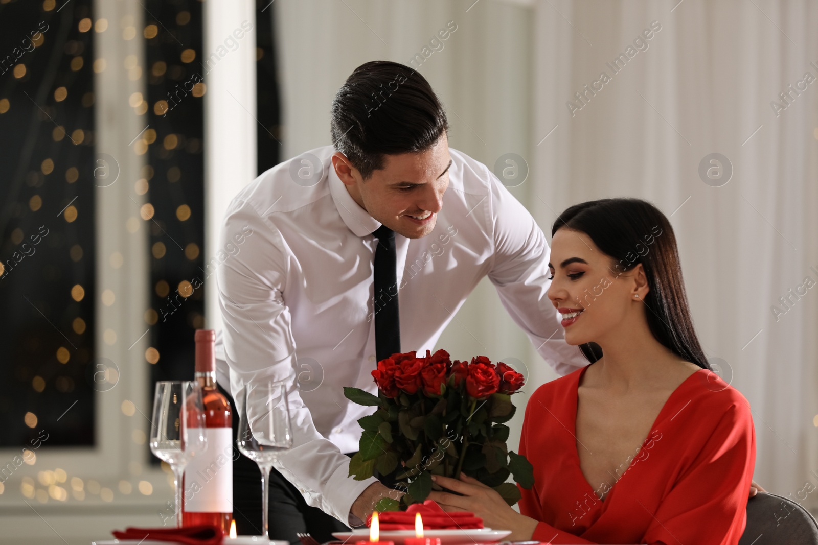 Photo of Man presenting roses to his beloved woman in restaurant. Romantic Valentine's day dinner