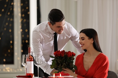 Photo of Man presenting roses to his beloved woman in restaurant. Romantic Valentine's day dinner