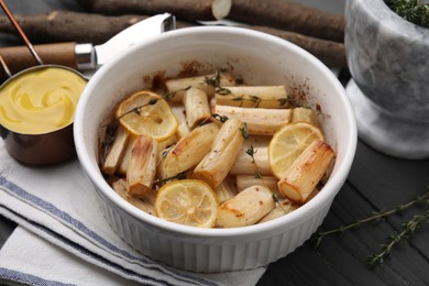Photo of Dish with baked salsify roots, lemon and thyme on black wooden table