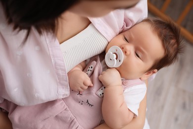 Mother holding her cute little baby with pacifier indoors, above view