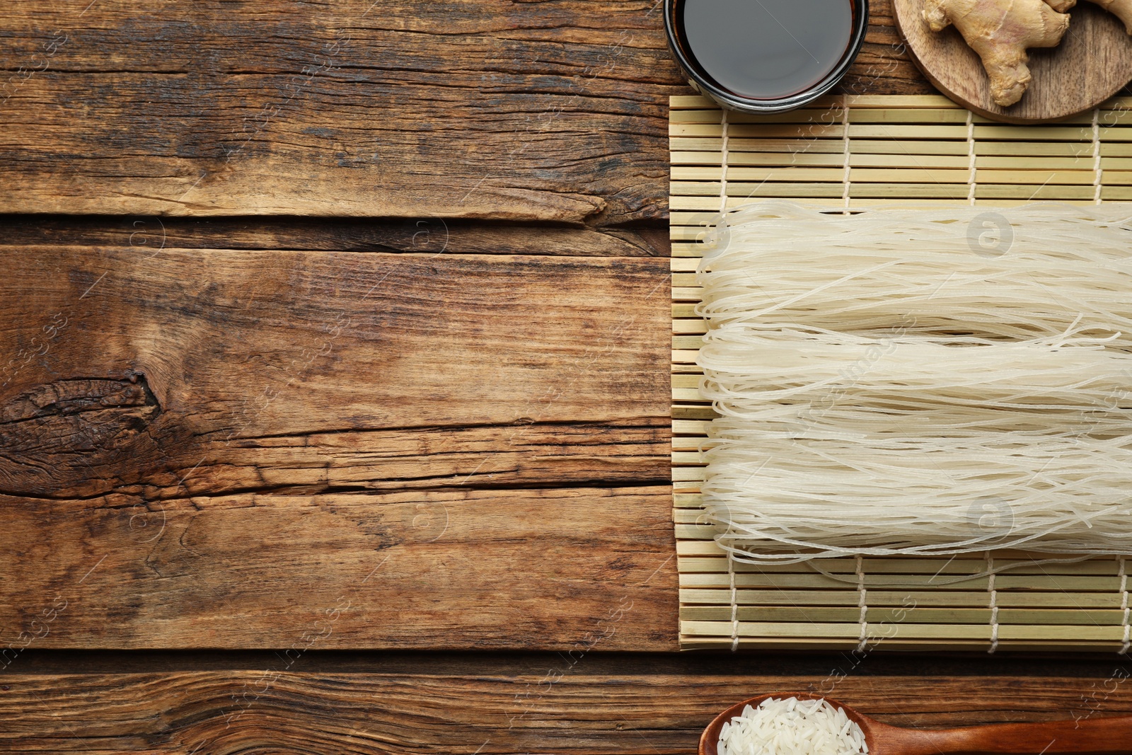 Photo of Flat lay composition with uncooked rice noodles, soy sauce and ginger on wooden table. Space for text