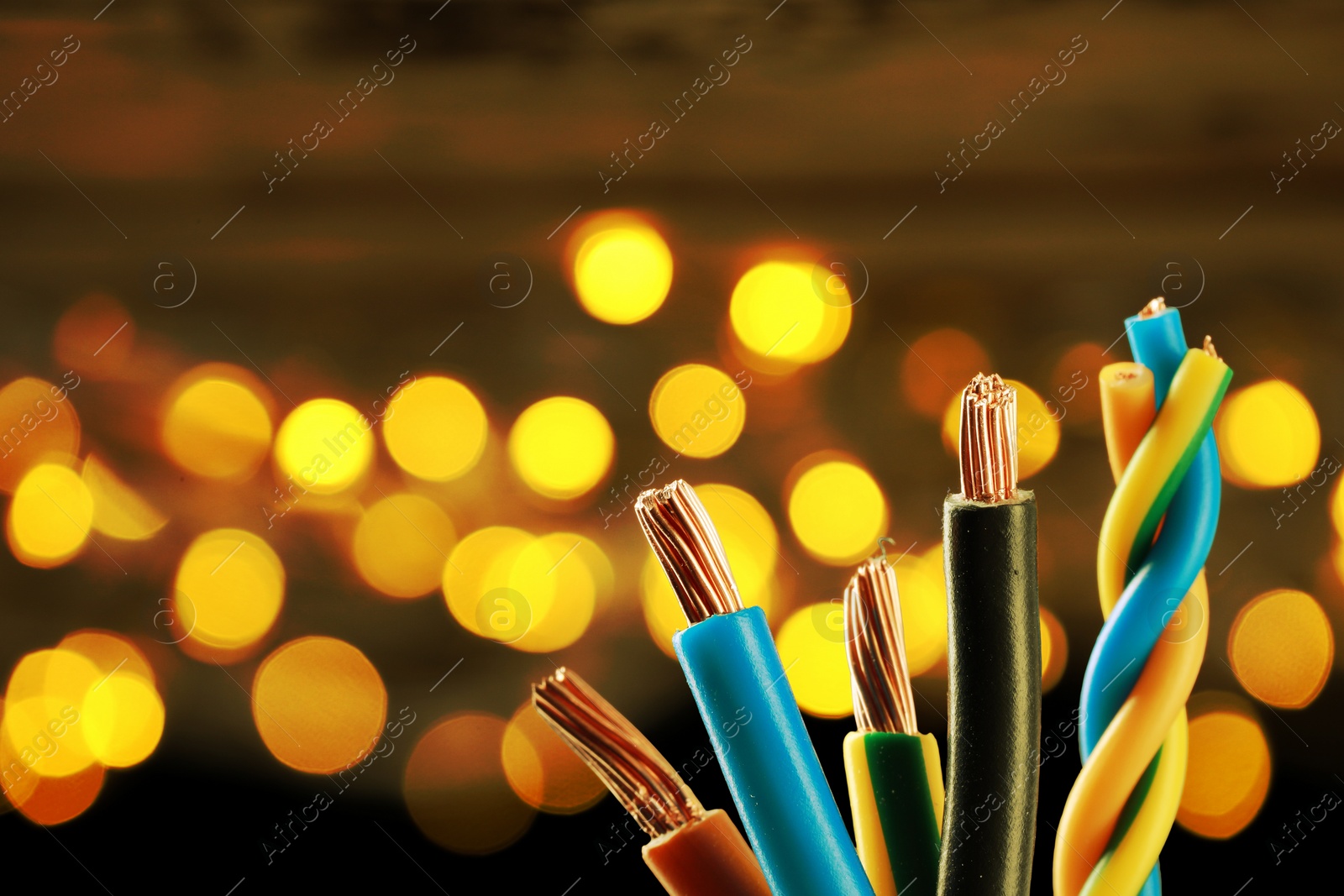 Image of Colorful electrical wires against background with blurred lights, closeup. Space for text