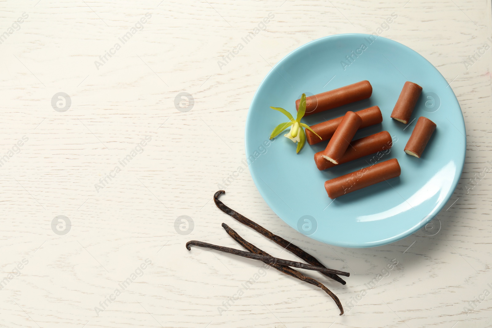 Photo of Glazed curd cheese bars, vanilla pods and flower on white wooden table, top view. Space for text