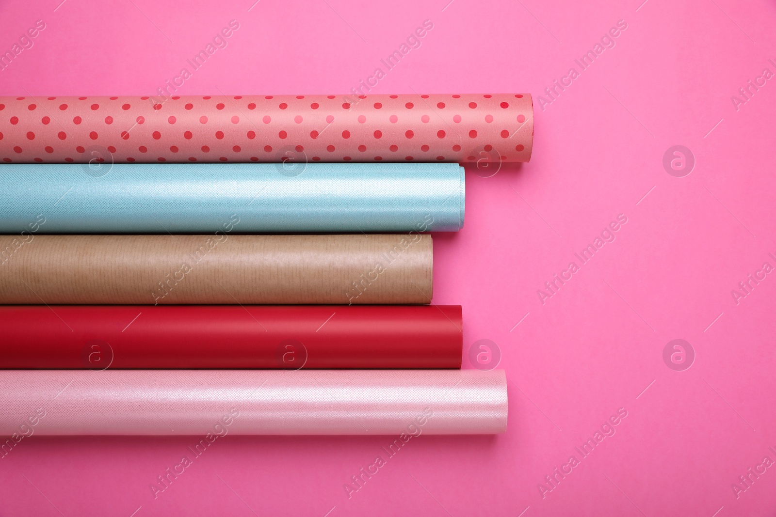 Photo of Rolls of colorful wrapping paper on pink background, flat lay