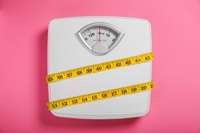 Weight loss concept. Scales and measuring tape on pink background, top view