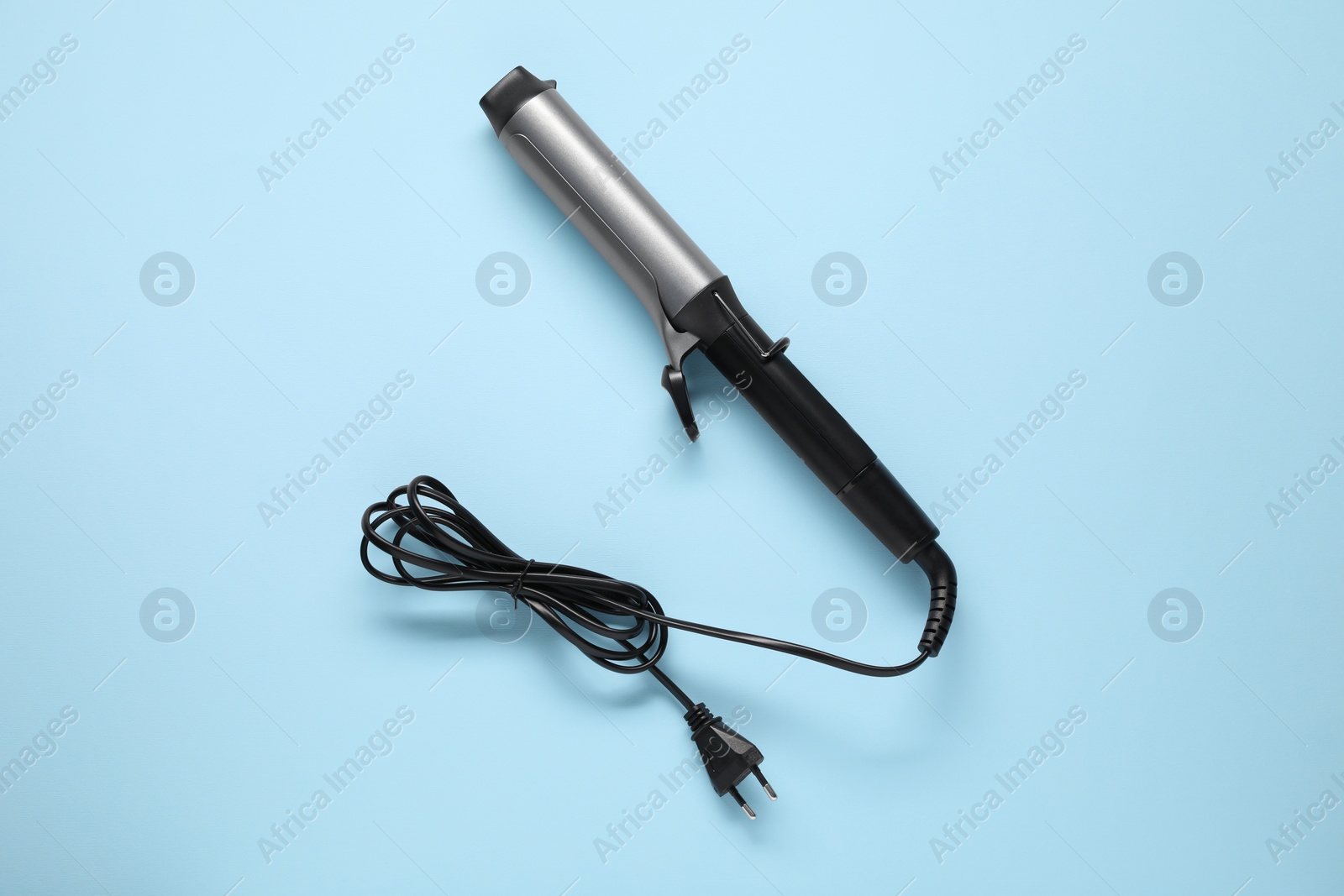 Photo of One curling iron on light blue background, top view. Hair styling appliance
