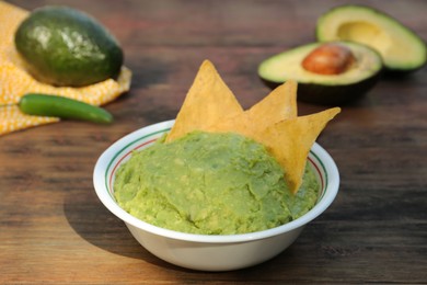 Photo of Delicious guacamole made of avocados with nachos on wooden table