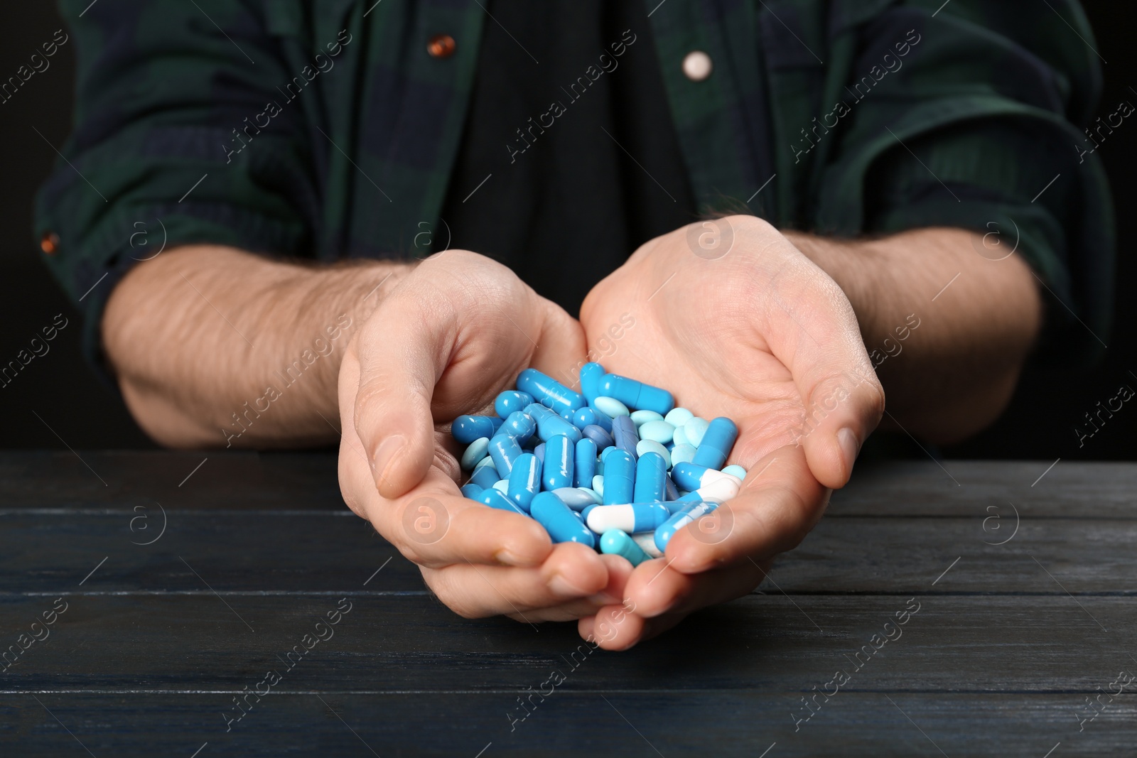 Photo of Man holding different pills in hands at table, closeup