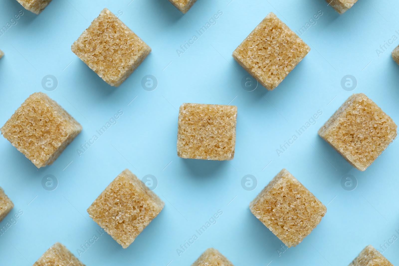 Photo of Brown sugar cubes on light blue background, flat lay