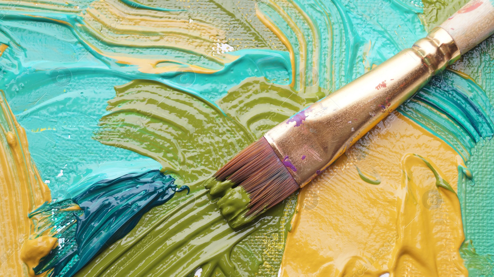 Photo of Brush on artist's palette with mixed paints, top view