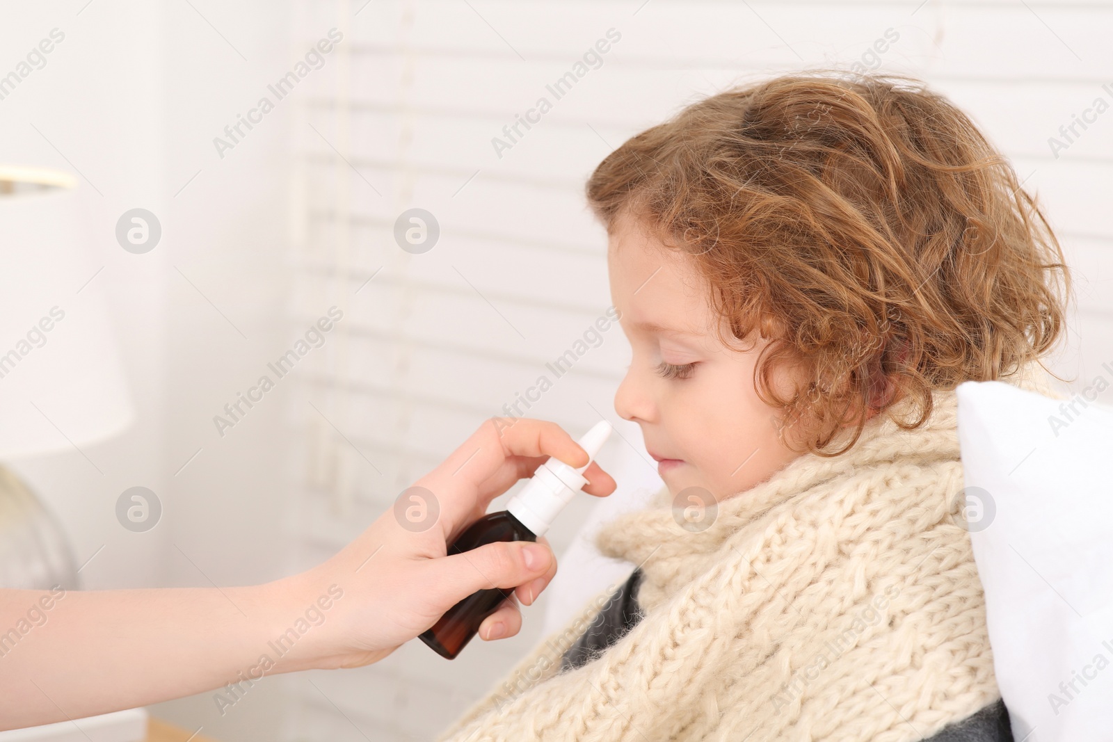 Photo of Mother using nasal spray to treat her little son indoors, closeup