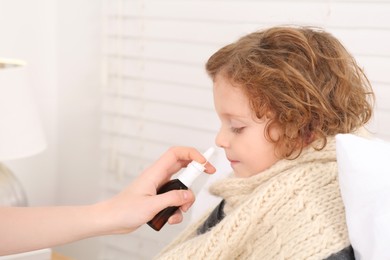 Mother using nasal spray to treat her little son indoors, closeup