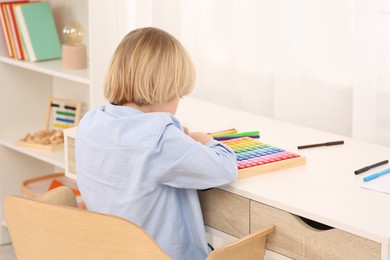Photo of Little boy playing with colorful wooden cubes at desk in room. Home workplace