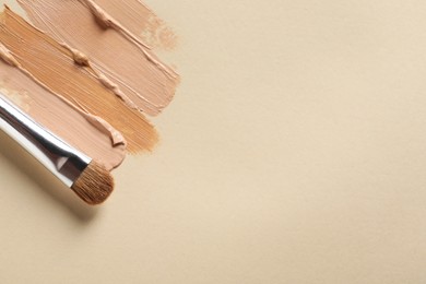 Photo of Samples of skin foundation and makeup brush on beige background, top view. Space for text