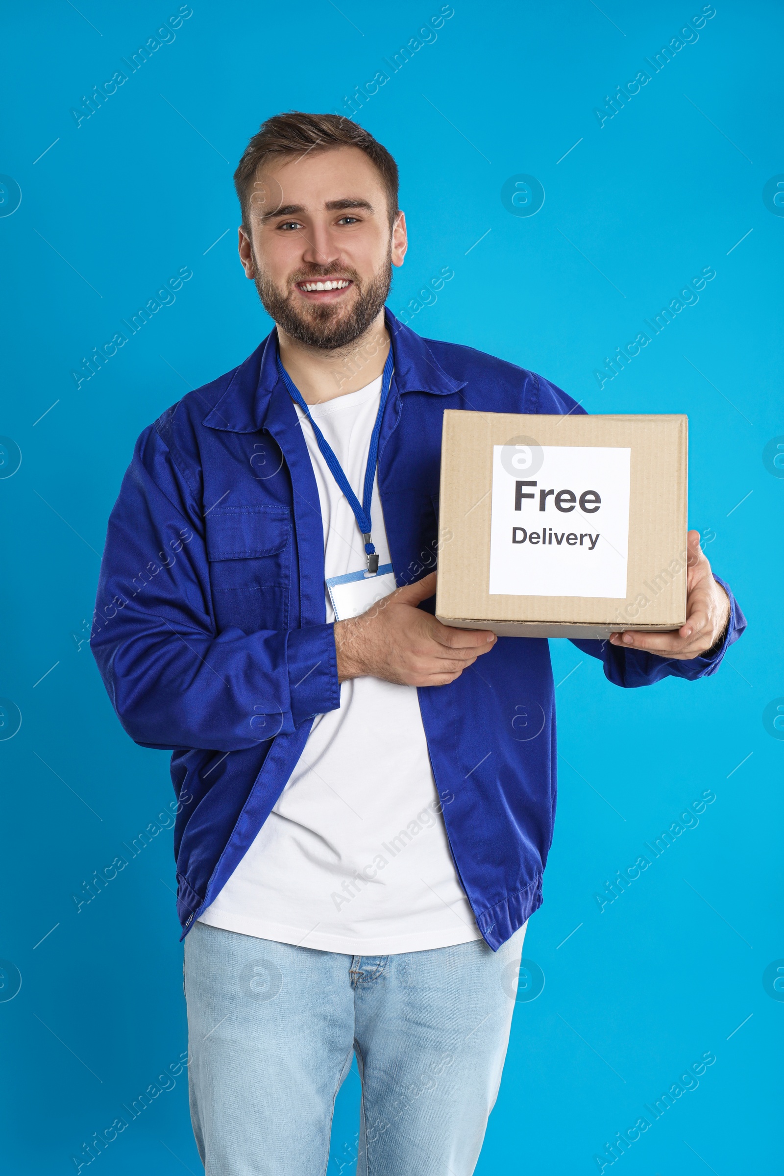 Photo of Male courier holding parcel with sticker Free Delivery on light blue background