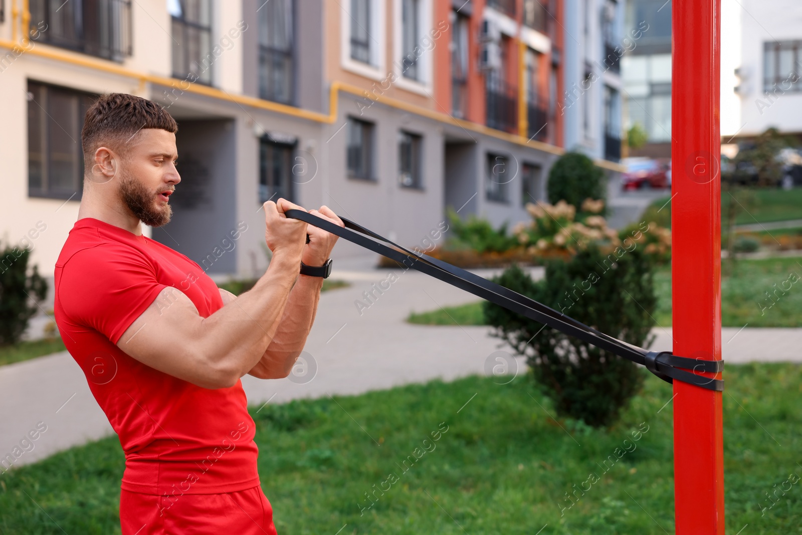 Photo of Muscular man doing exercise with elastic resistance band outdoors