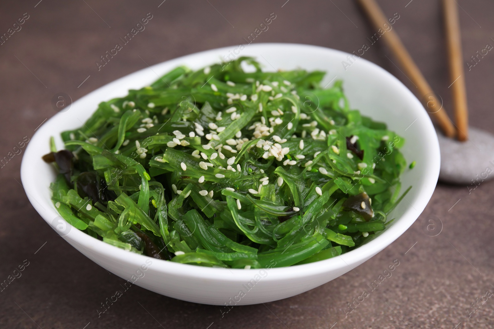 Photo of Tasty seaweed salad in bowl served on brown table, closeup