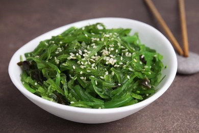 Photo of Tasty seaweed salad in bowl served on brown table, closeup