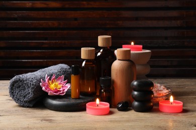 Photo of Different aromatherapy products, spa stones, towel and flower on wooden table