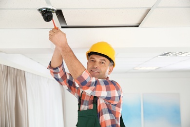 Electrician with screwdriver repairing CCTV camera indoors