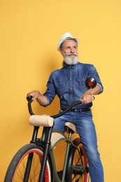 Portrait of handsome mature man with bicycle on color background