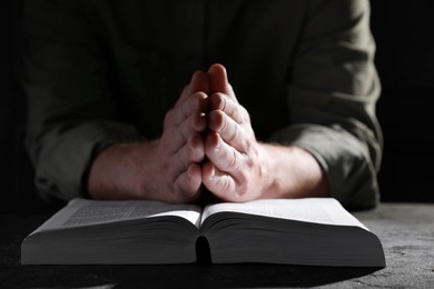 Photo of Religion. Christian man praying over Bible at table, closeup