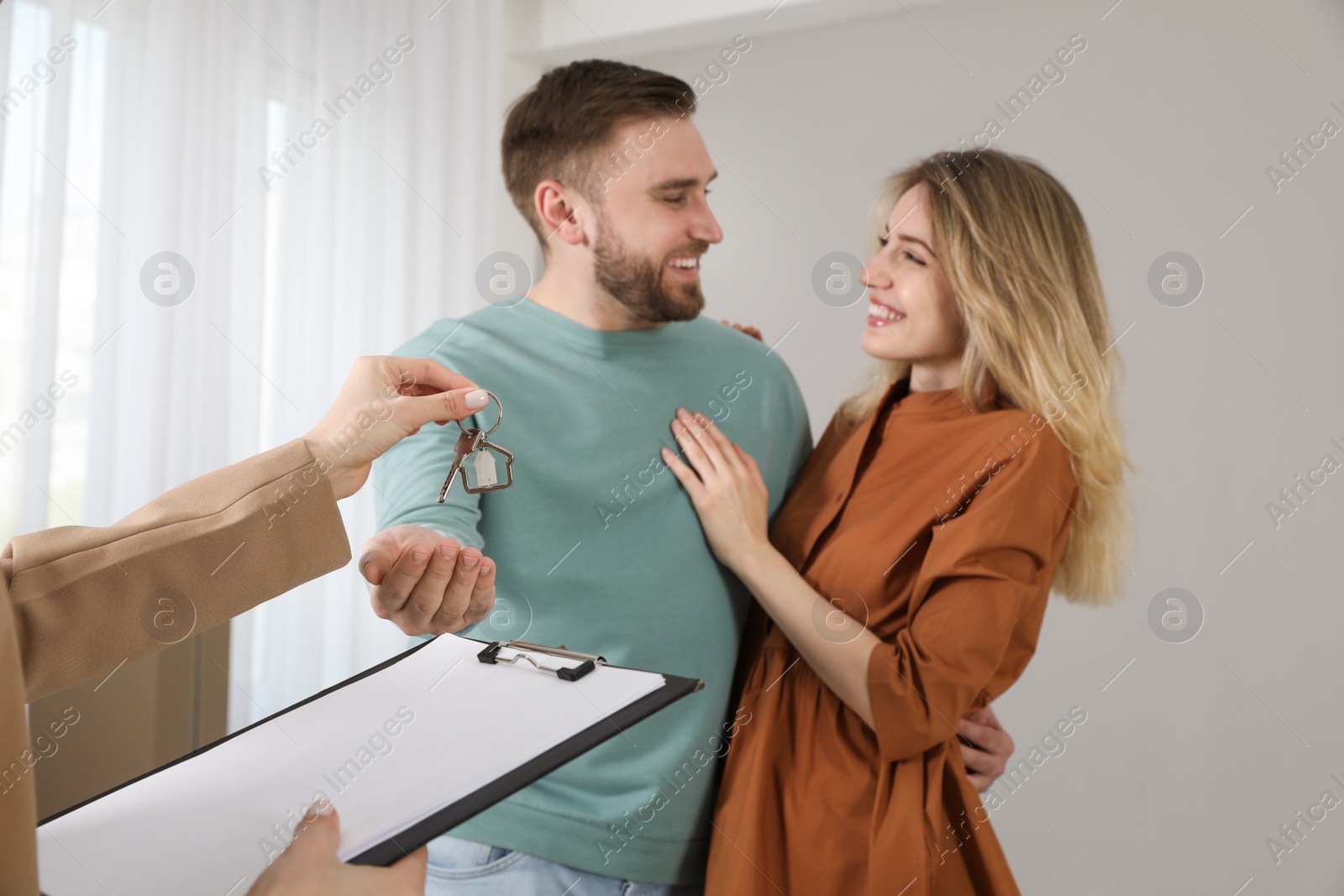 Photo of Real estate agent giving key to happy young couple in new house, focus on hands